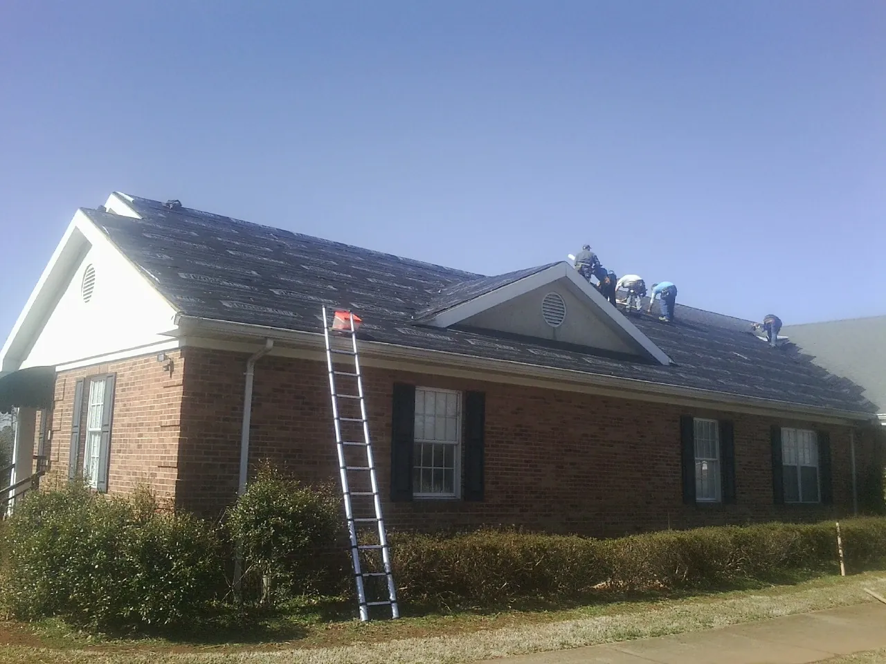 Crew tearing shingles off a brick ranch roof with a ladder set — Metal Roof Repair work by our crew in San Mateo