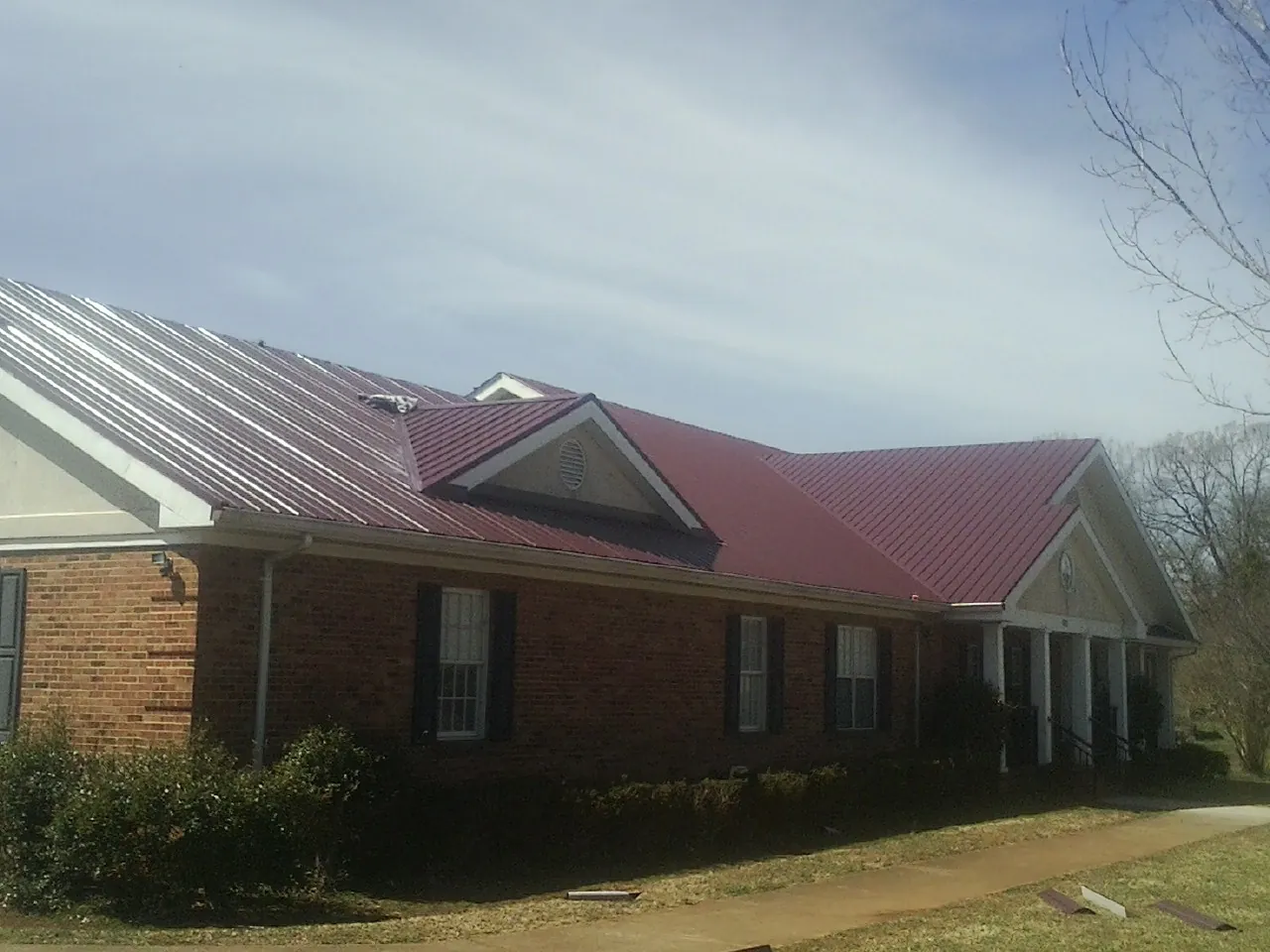 Red metal roof with gabled entries on a long brick building, from a Hail Damage Roof Repair job in San Mateo