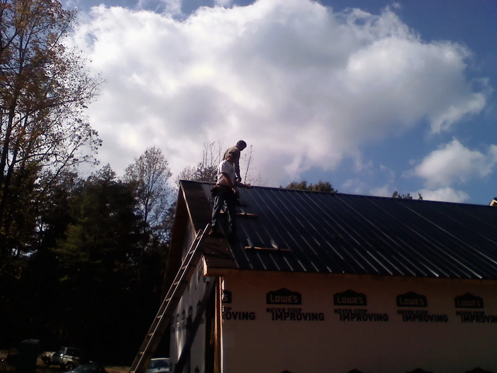 Roofer fastening dark metal panels high against a cloudy sky, from a Roof Inspection job in San Mateo
